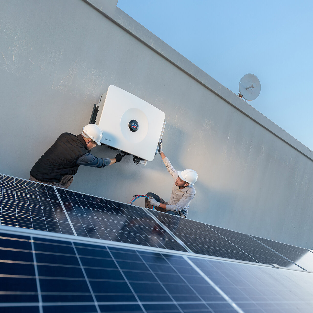 Two installers are installing a Sunny Tripower 125 for a commercial system with solar modules.